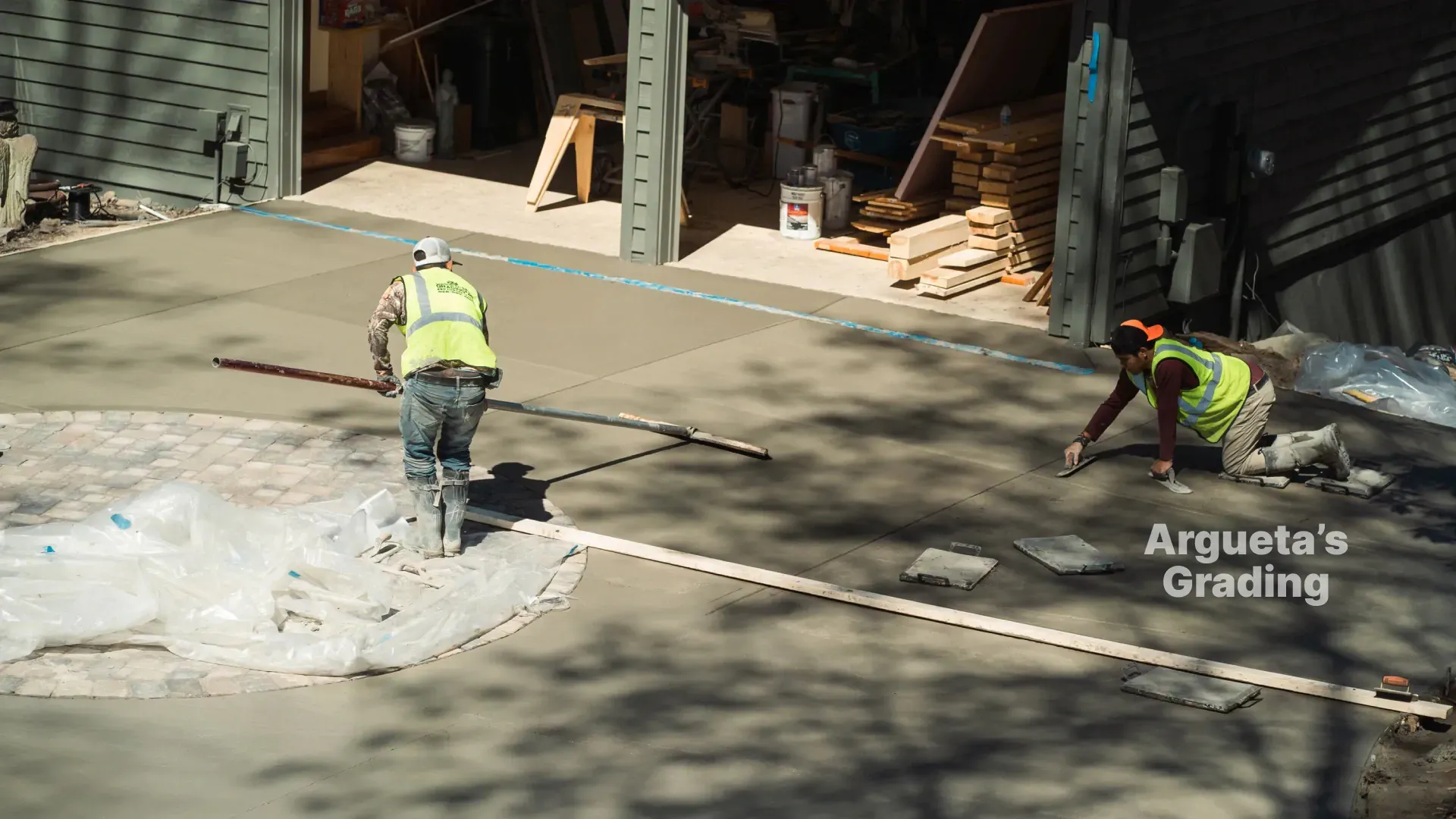 Construction workers leveling fresh concrete driveway.