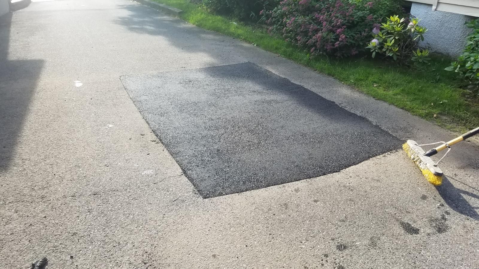 Asphalt patch on a paved surface; a yellow brush is in the bottom right corner.