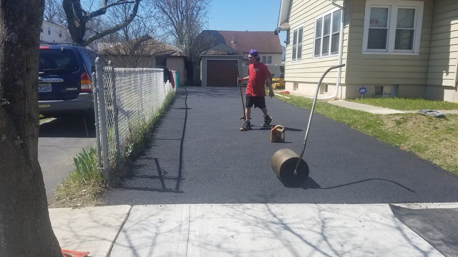 A man rolls a dark driveway sealer on a freshly paved asphalt driveway