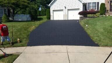 A freshly paved black asphalt driveway in front of a white house