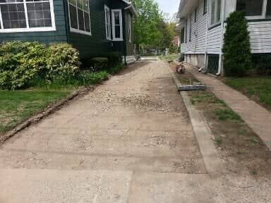A dirt driveway between two houses, with exposed aggregate.  The driveway is under construction, and the edges have grass.