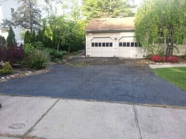 A paved driveway leading to a two-car garage. The garage doors are white, and the driveway is dark asphalt.