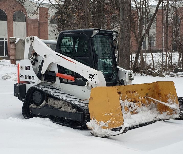 White Bobcat track loader with a yellow plow clearing snow, likely outdoors in a winter setting.