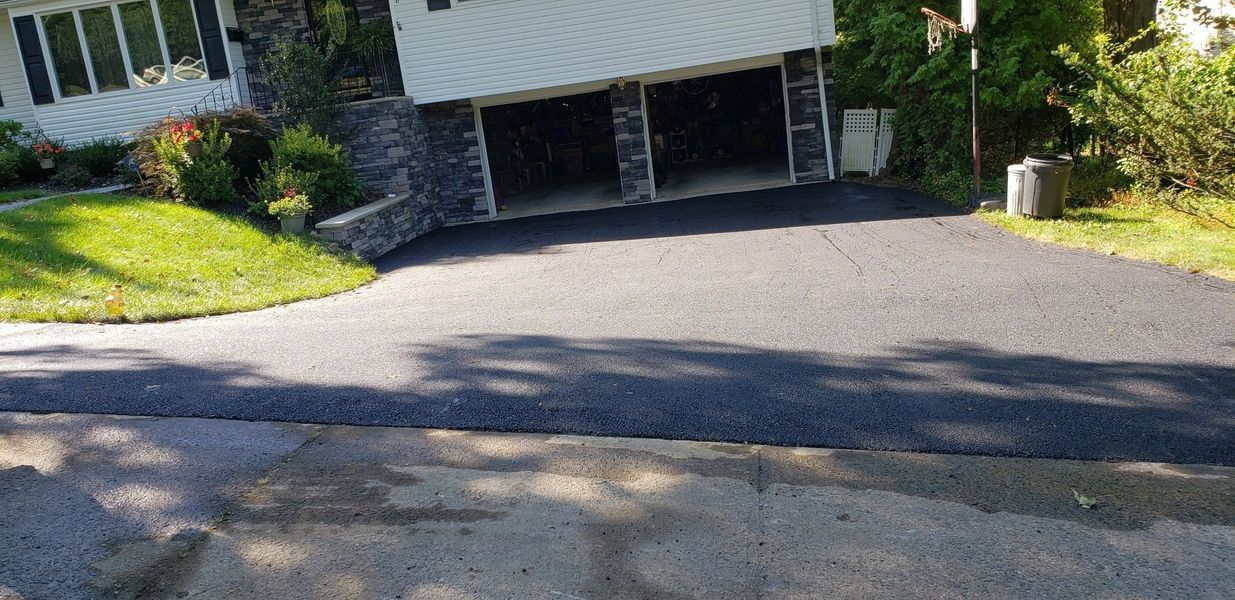 Driveway in front of a house with two garage doors.  Green grass and trees are visible.