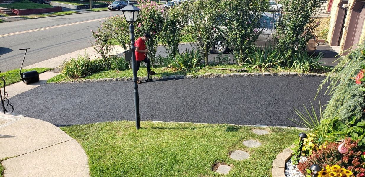A person near a red object and a black pole on a driveway, a car and a road are in the background.