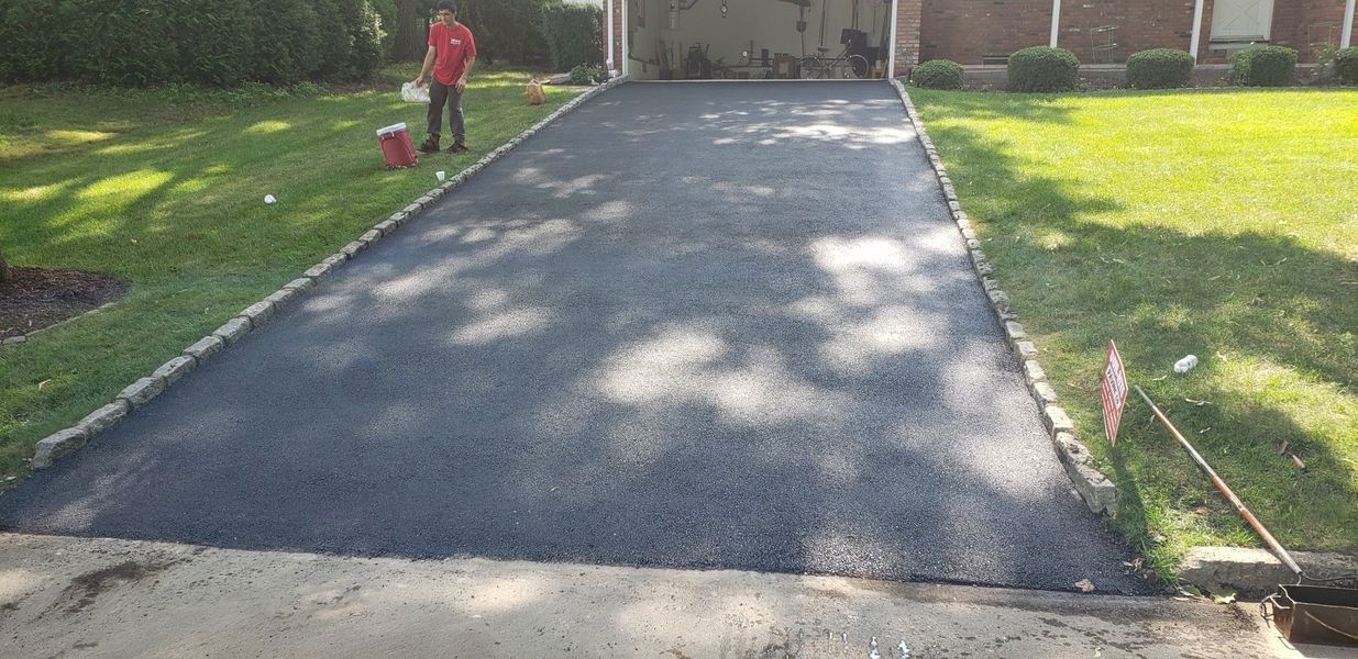 A newly paved asphalt driveway with green grass on either side.