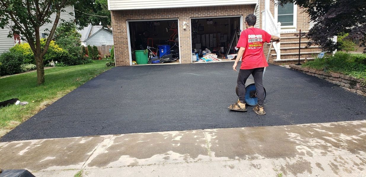 Person riding a one-wheel device on a newly paved driveway, in front of a garage. They wear a red shirt and black pants.