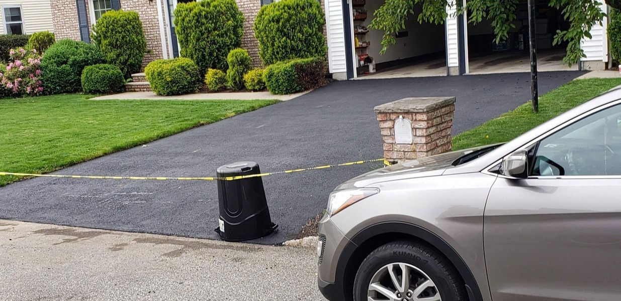 A silver car parked next to a black object with yellow caution tape on a driveway