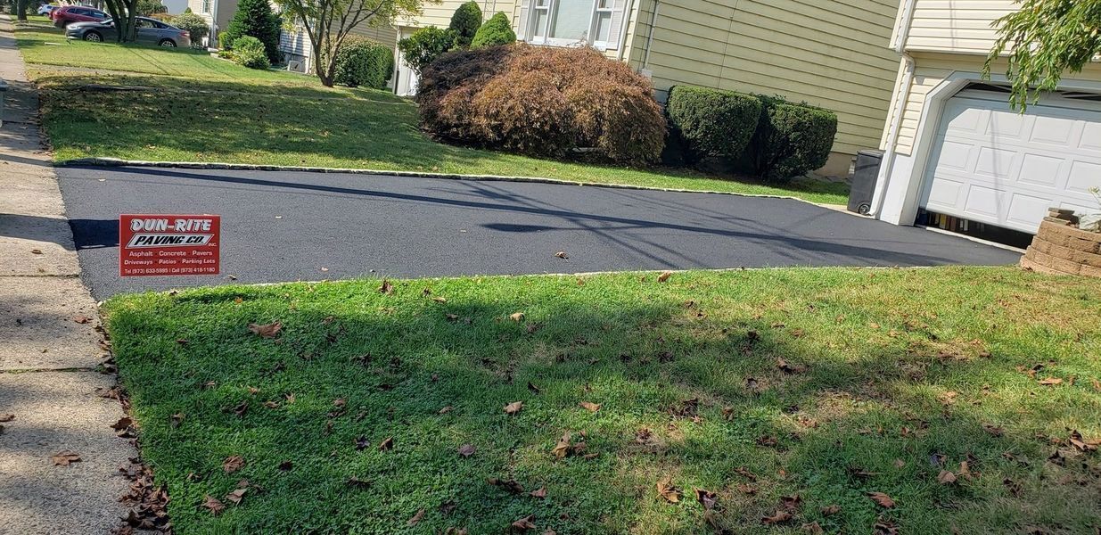 Asphalt driveway, grass, and sidewalk in front of a house with a lawn service sign.