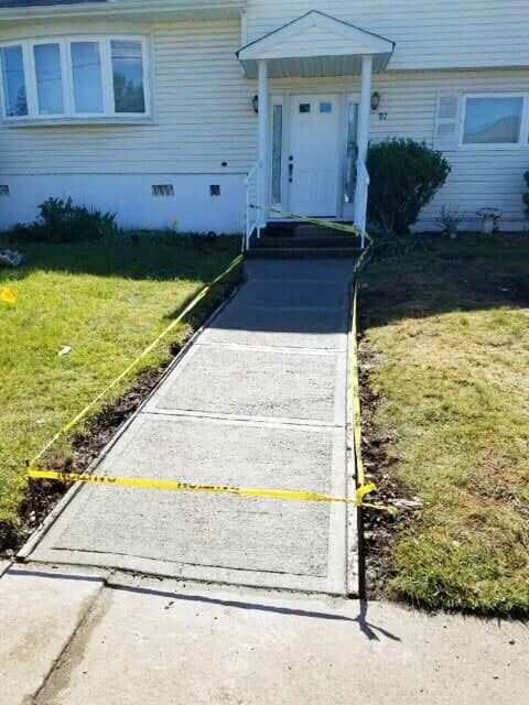 Newly poured concrete walkway leading to a house with a white door, marked off with yellow caution tape.