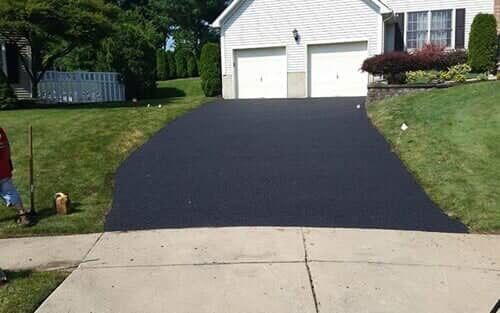 Freshly paved black asphalt driveway leading to a white house with two garage doors