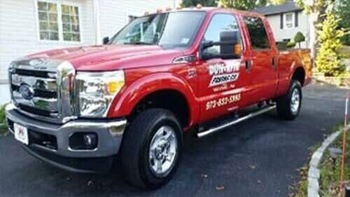 Red Ford pickup truck parked on a driveway. The truck has the business name 