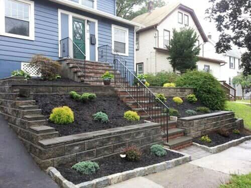 A blue house with brick steps leading up to the front door, with tiered landscaping in front.