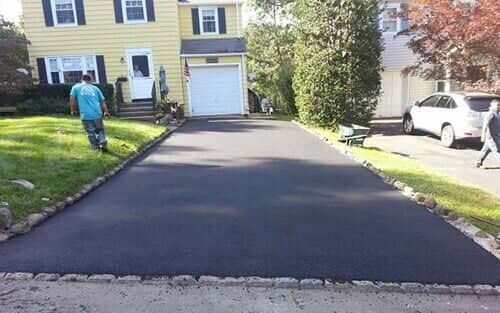 Newly paved asphalt driveway in front of a yellow house with a garage