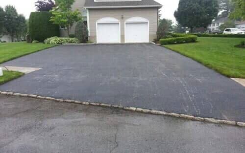 Asphalt driveway leading to a two-car garage with white doors. Green lawn surrounds the driveway.