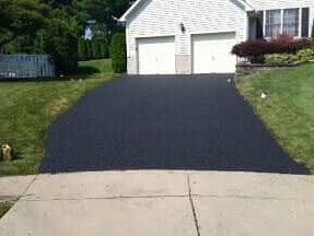 Freshly paved black asphalt driveway leading to a white house with a green lawn.