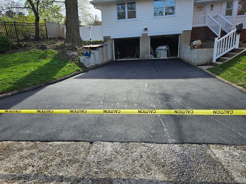 Freshly paved asphalt driveway with caution tape in front of a two-car garage.