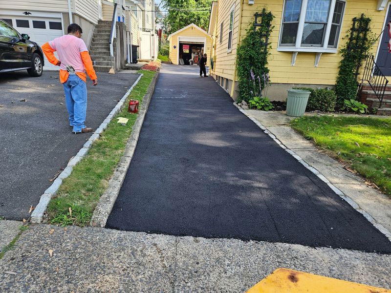 A newly paved asphalt driveway with a worker in orange and blue standing near the edge.