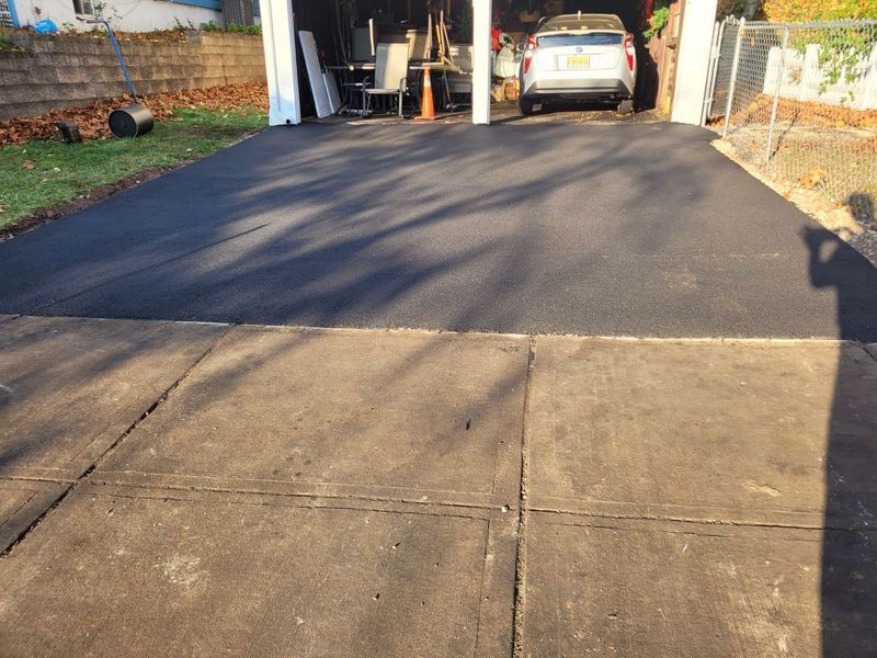 Newly paved asphalt driveway leading to a garage, contrasted by a gray concrete approach.