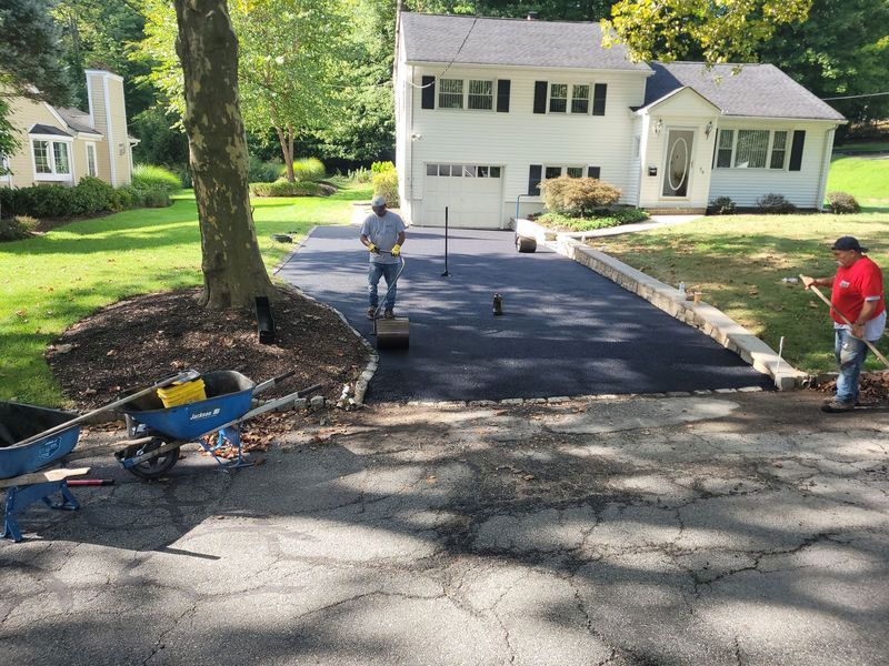 Workers paving a driveway in front of a white house. 