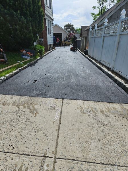 Newly paved driveway, dark black asphalt contrasts with light concrete entry. Workers in the distance.