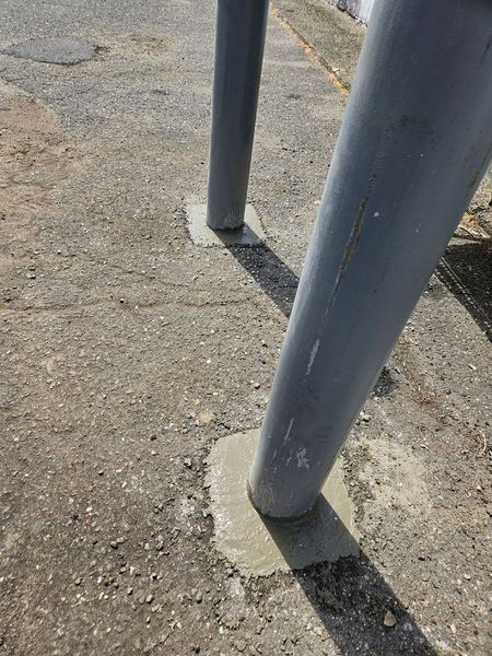 Gray metal poles secured to a concrete surface with small concrete patches, casting shadows on the ground.