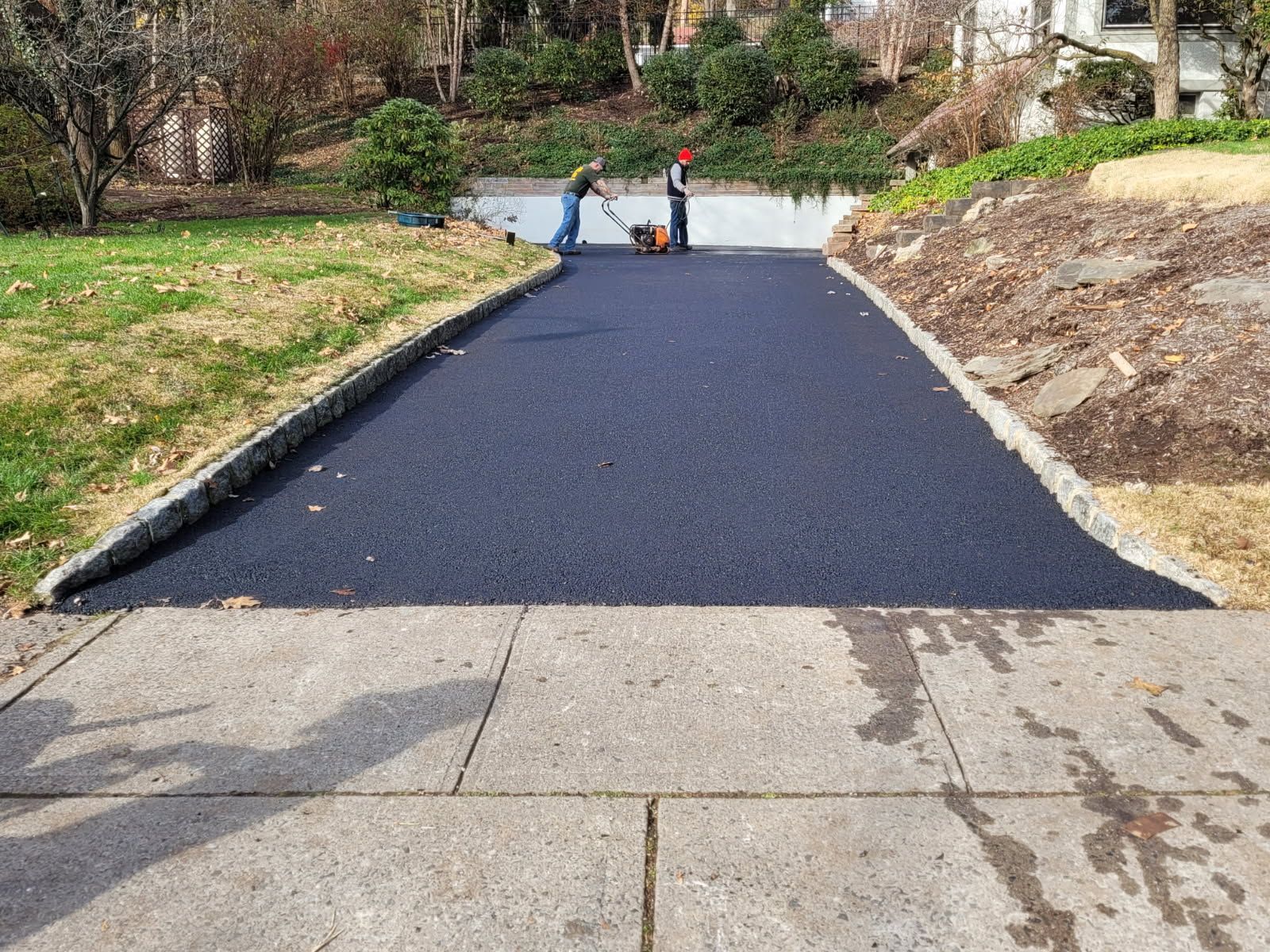 Newly paved asphalt driveway leading to a garage door; green grass and steps on the sides.