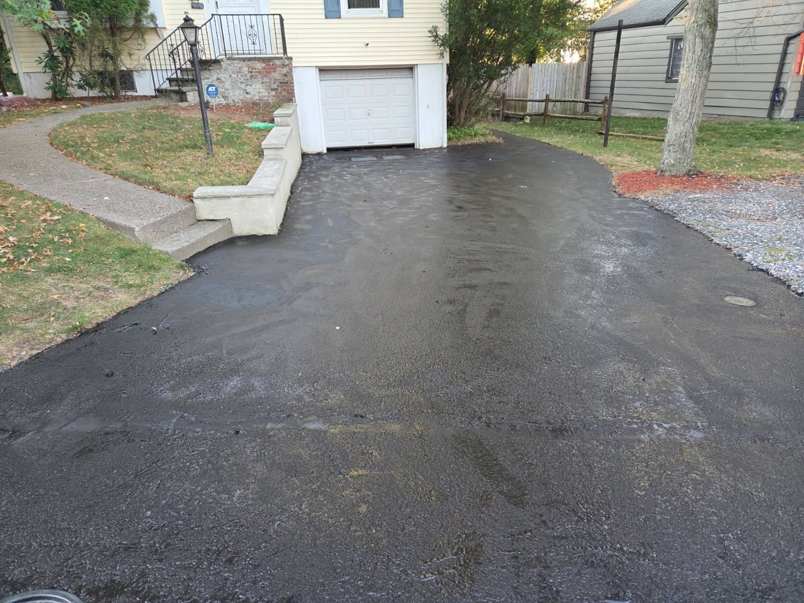 Asphalt driveway leading to a garage door, with a walkway on the left side of the house.