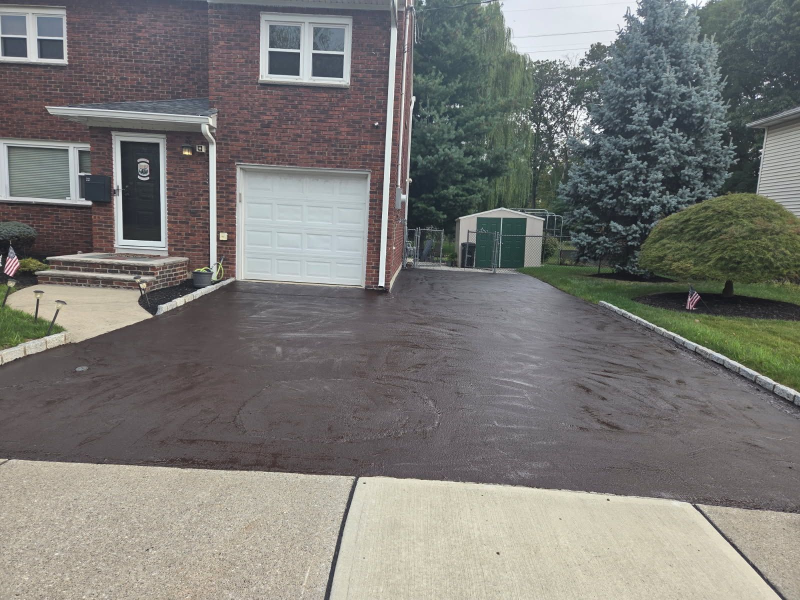Driveway leading to a garage door. Asphalt is wet. House and yard visible.