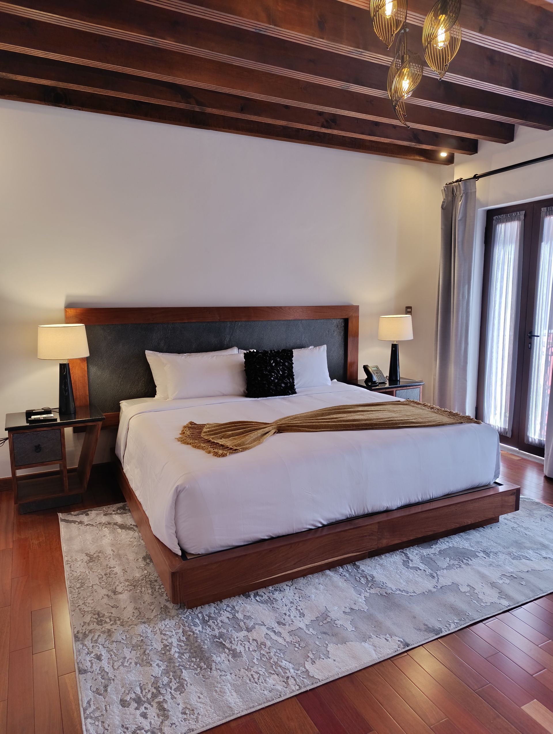Dormitorio de hotel de lujo con una cama King, pisos de madera y techo con vigas a la vista.