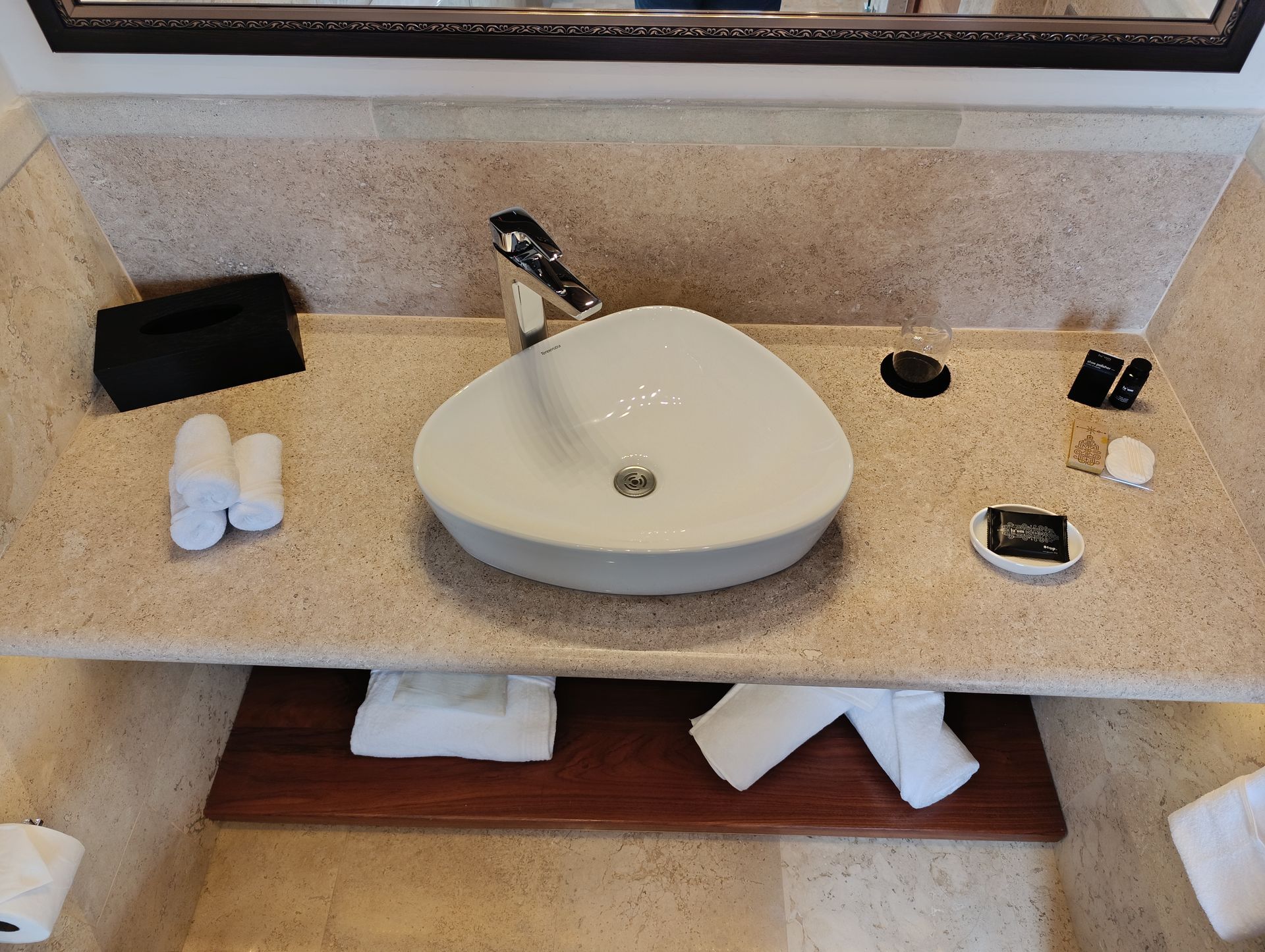 Mueble de baño con lavabo blanco en forma de corazón. Toallas y artículos de aseo blancos sobre la encimera beige.