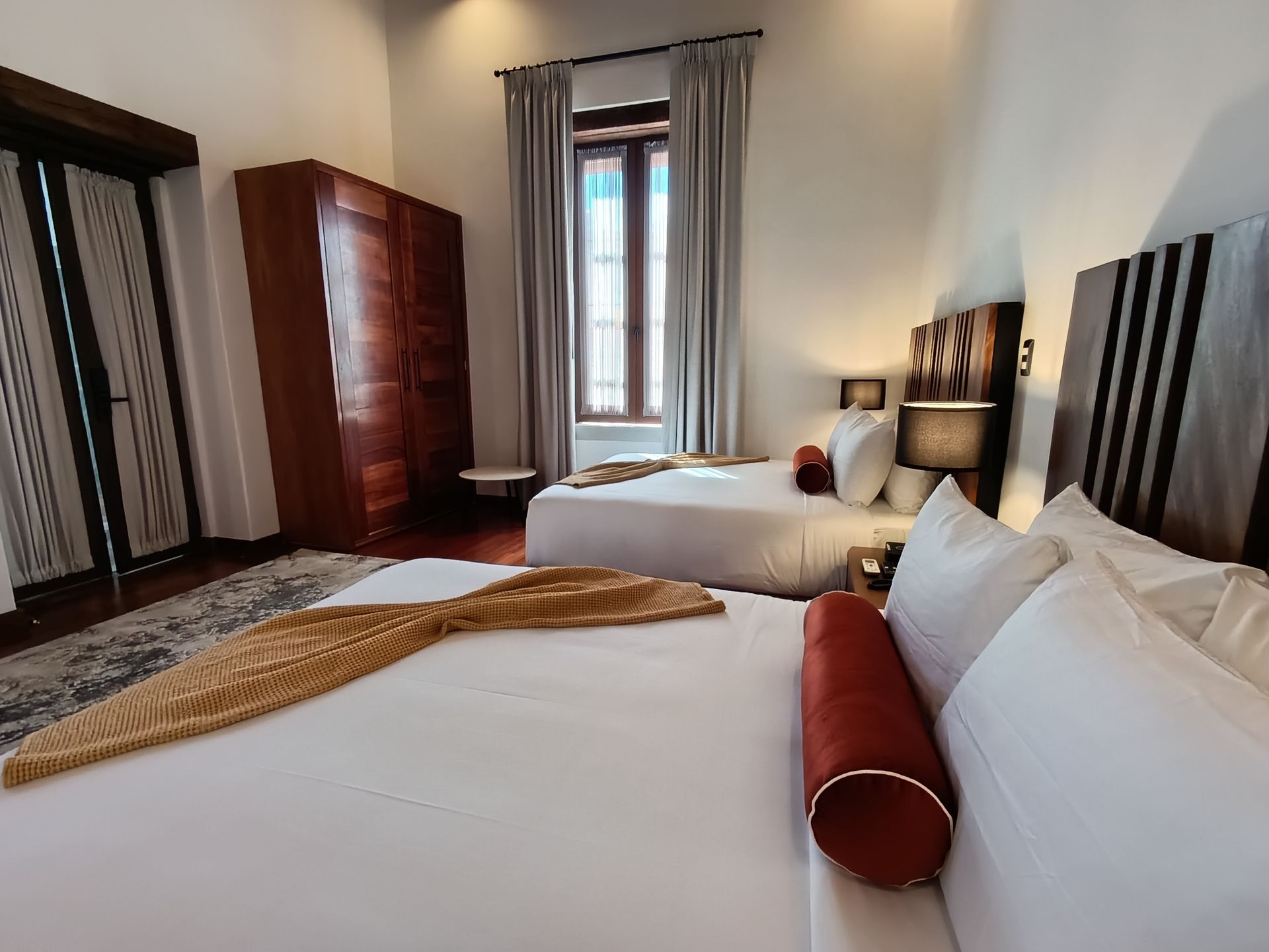 Dormitorio con dos camas, ventana, armario de madera y cojines decorativos.