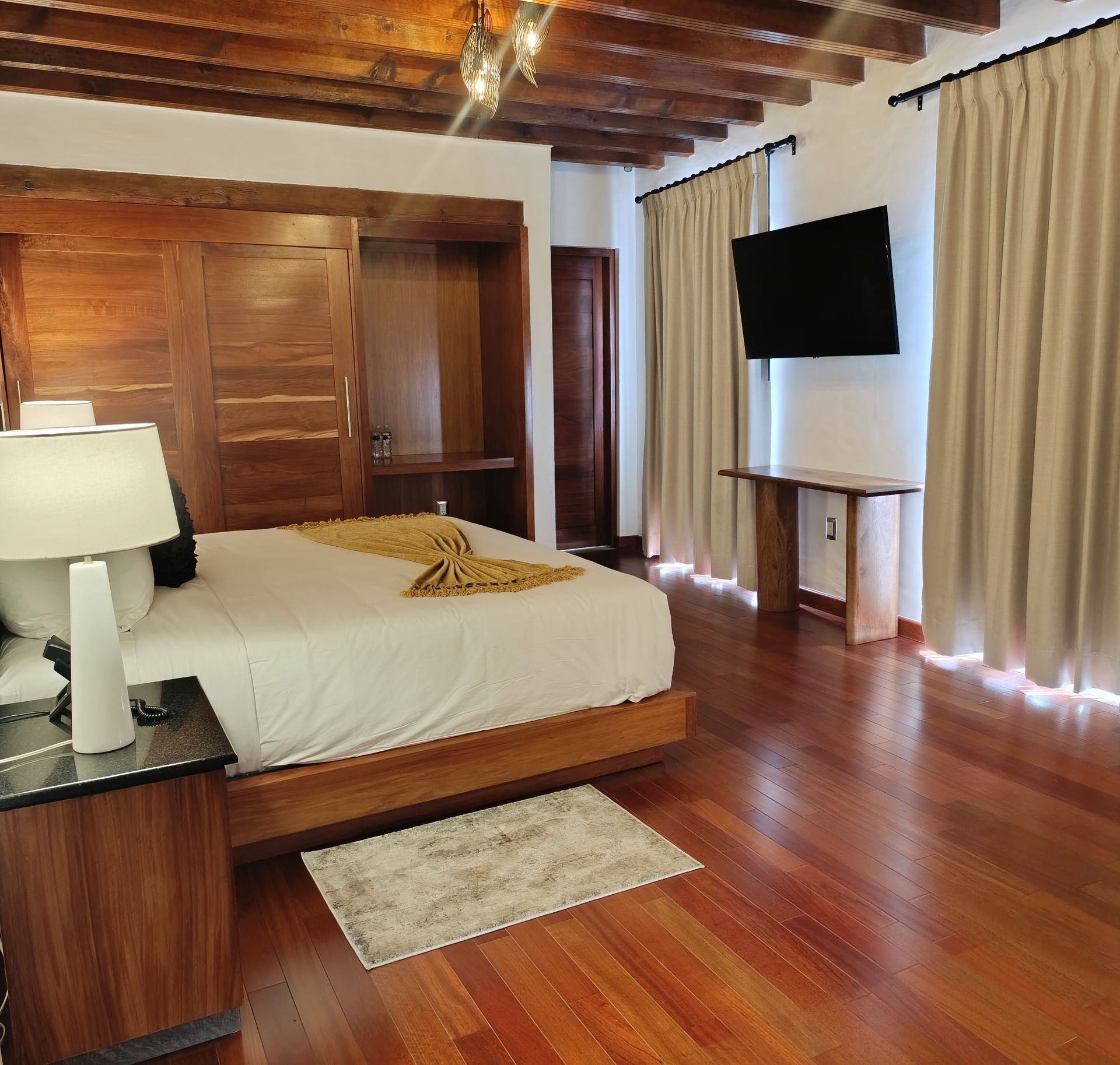 Dormitorio con cama, paredes y techo de madera. Hay un televisor colgado en la pared. El suelo es de madera.