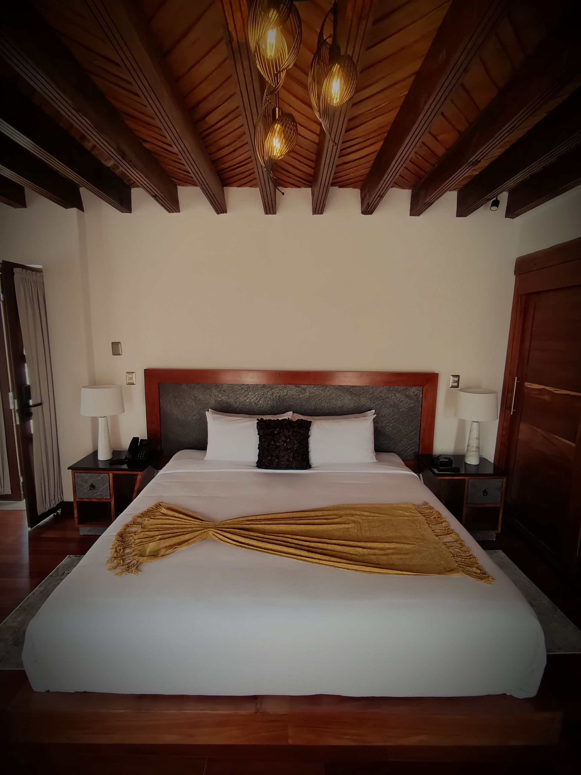 Dormitorio con cama grande, vigas de madera en el techo, paredes blancas y mesitas de noche.