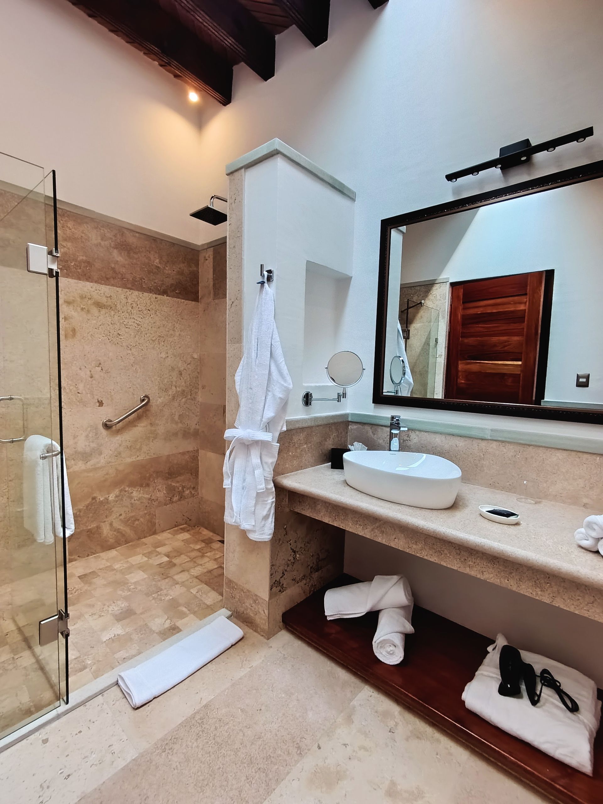 Baño con ducha de piedra, albornoz, lavabo y gran espejo.