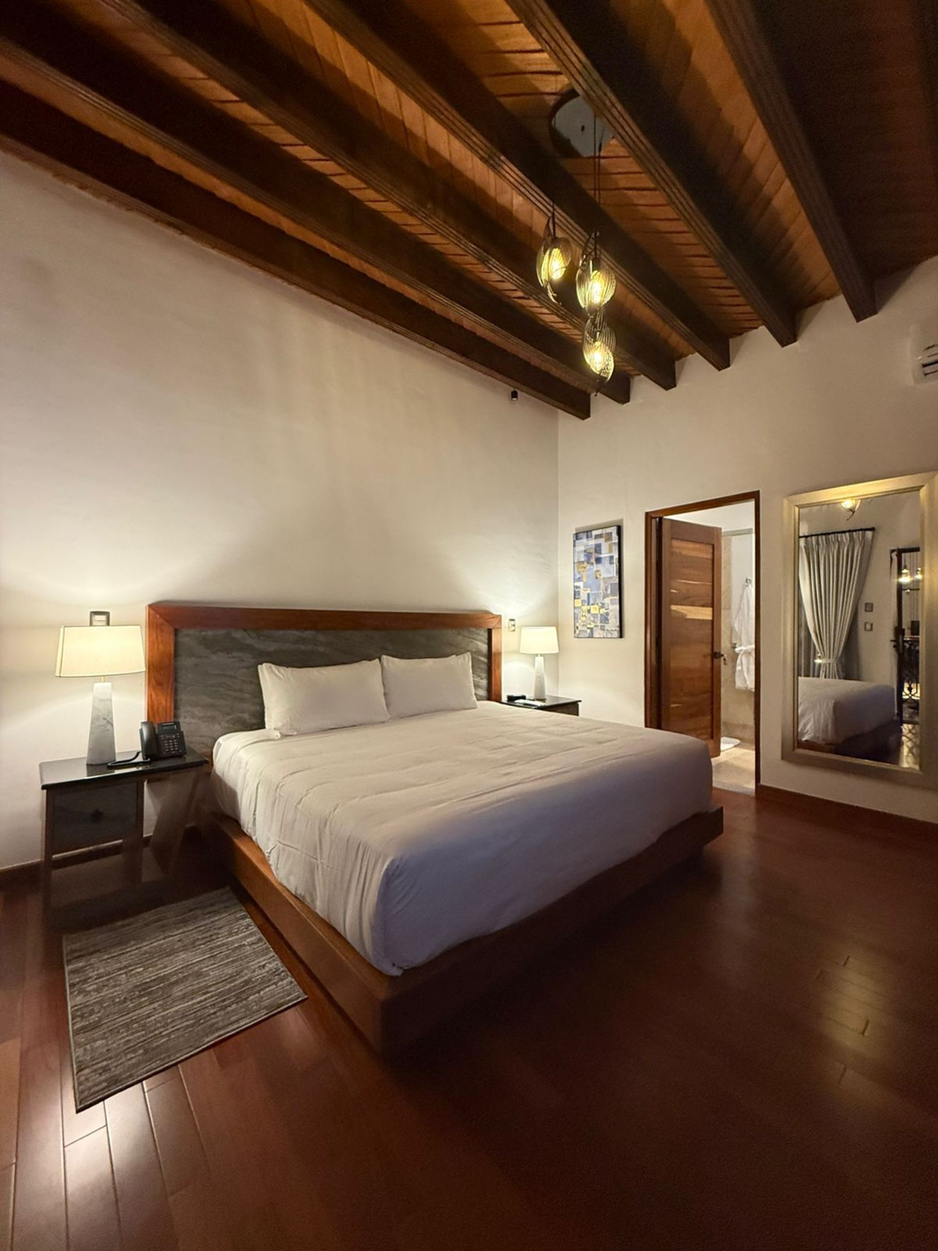 Dormitorio con estructura de cama de madera, pisos de madera y vigas de madera a la vista en el techo.