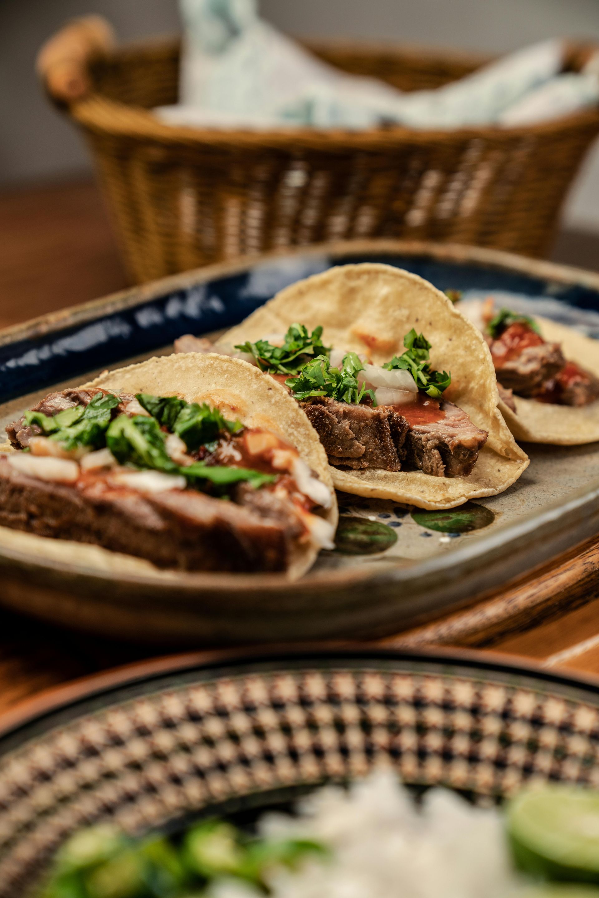 Tres tacos en un plato rectangular, con carne, cebolla, cilantro y salsa.