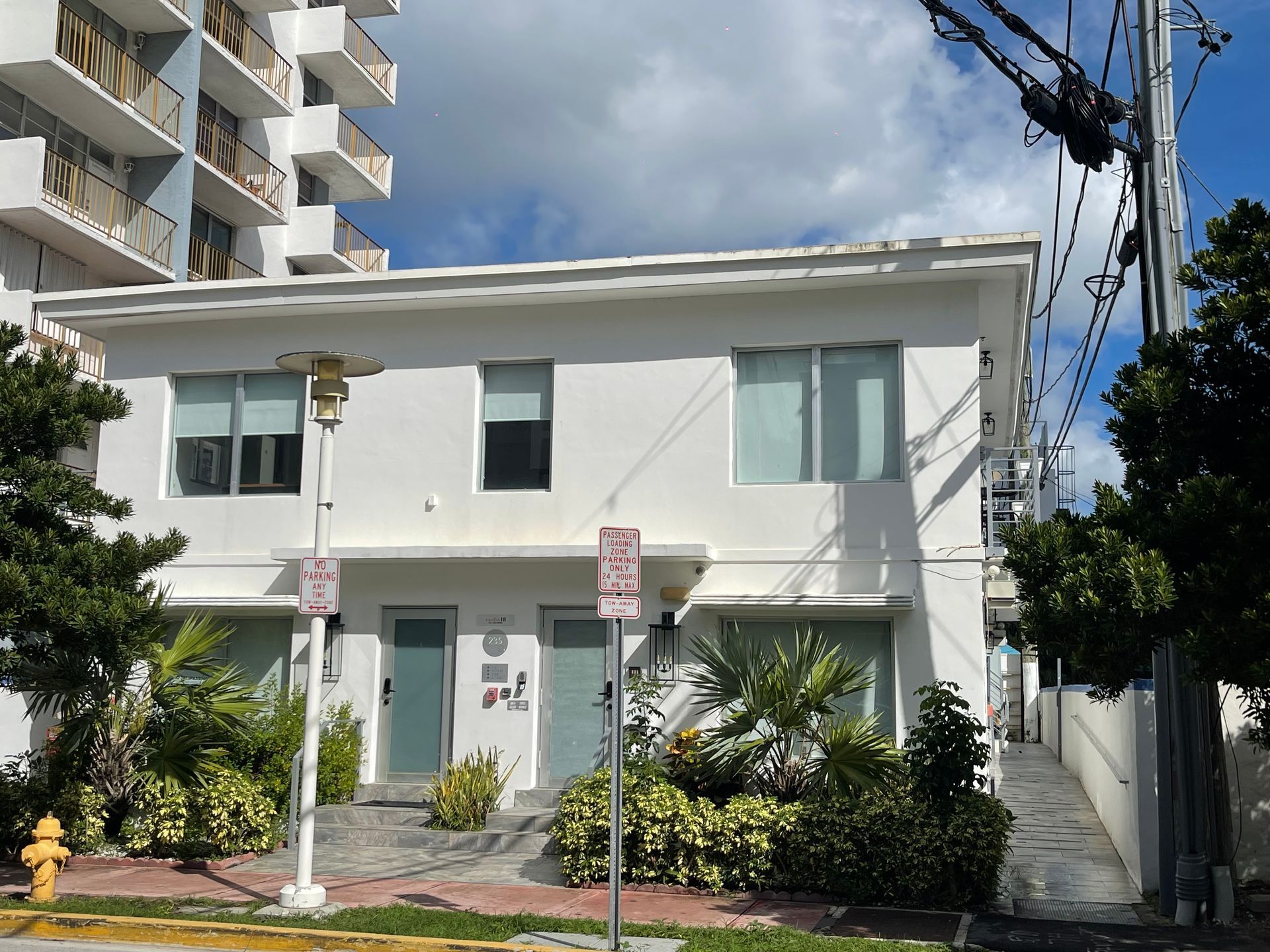 Two-story white building with teal doors and windows, under a sunny blue sky.