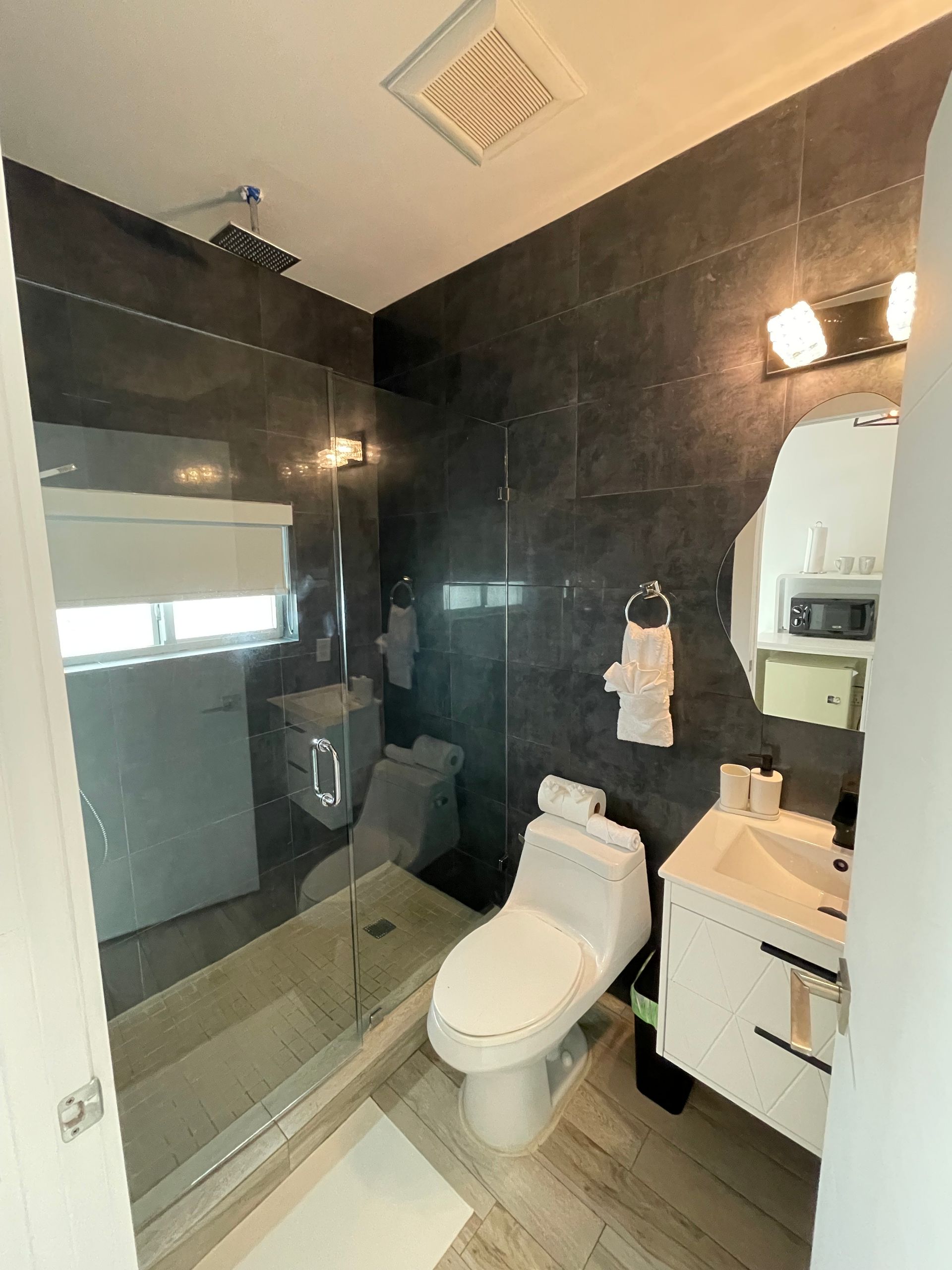 Modern bathroom with dark gray tile walls, a glass shower, and a white toilet and sink.