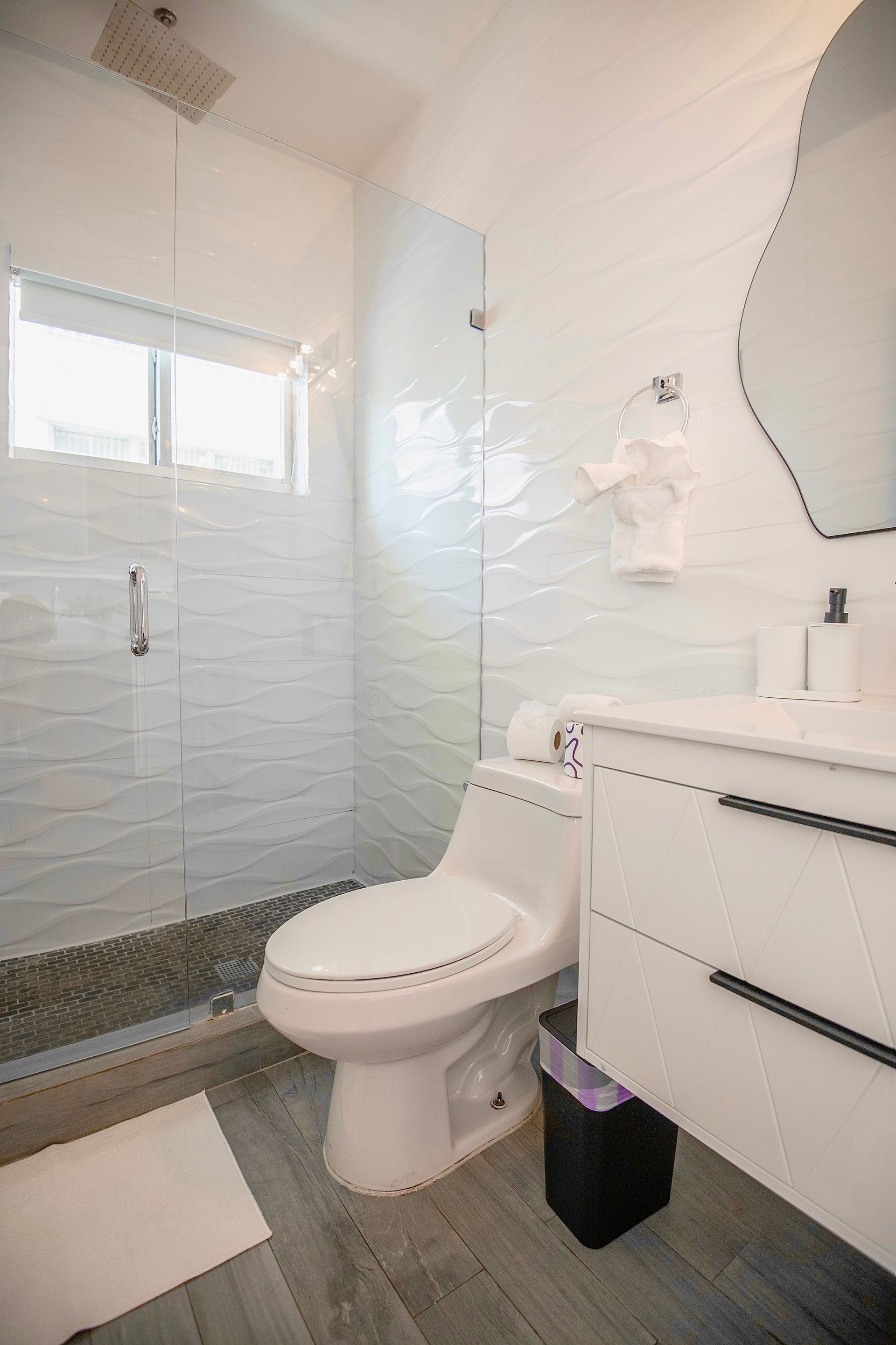 Bright white bathroom with textured wall tiles, glass shower, and modern vanity.