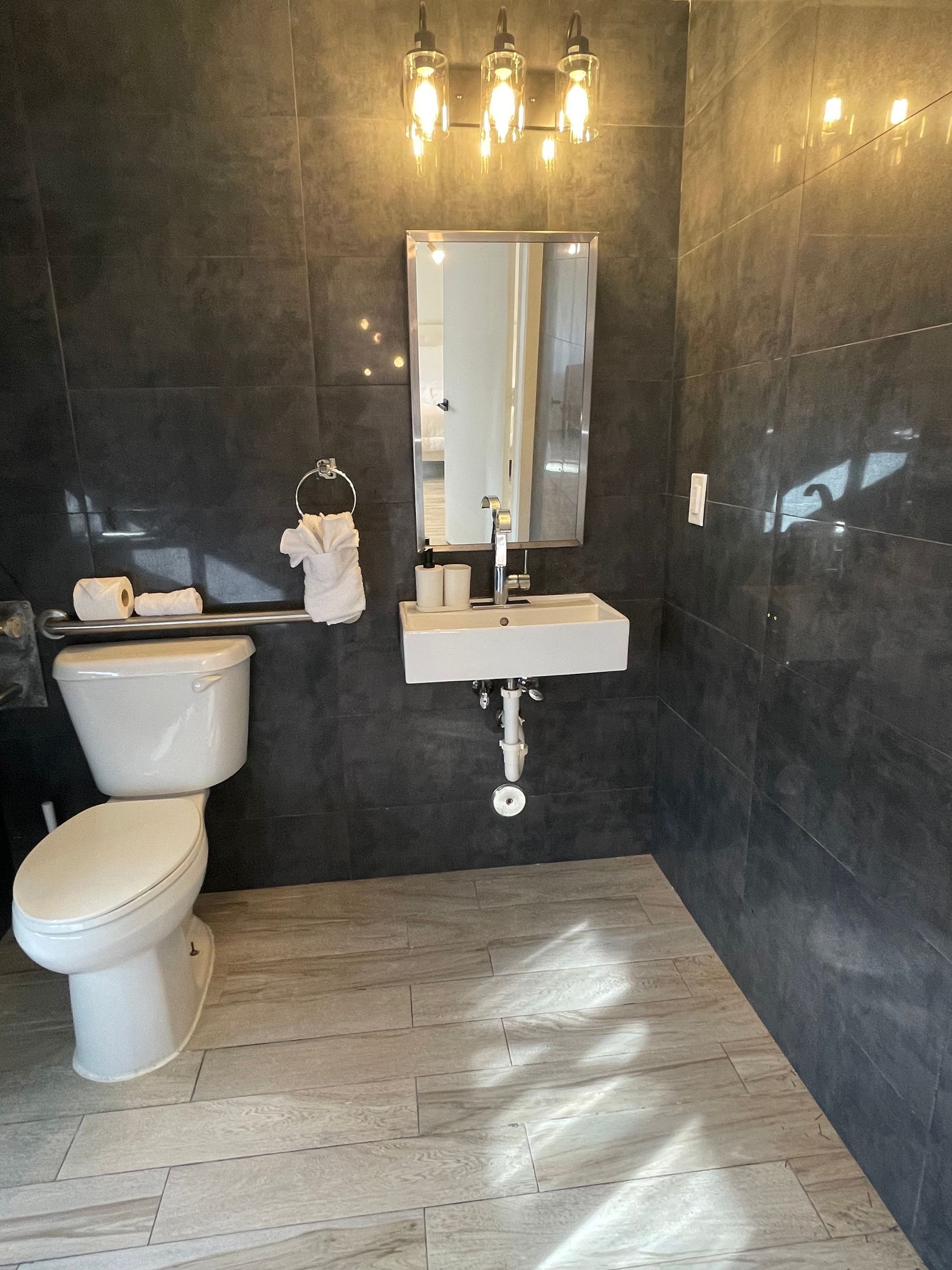 Small modern bathroom with white toilet, sink, mirror, and dark gray tiled walls.
