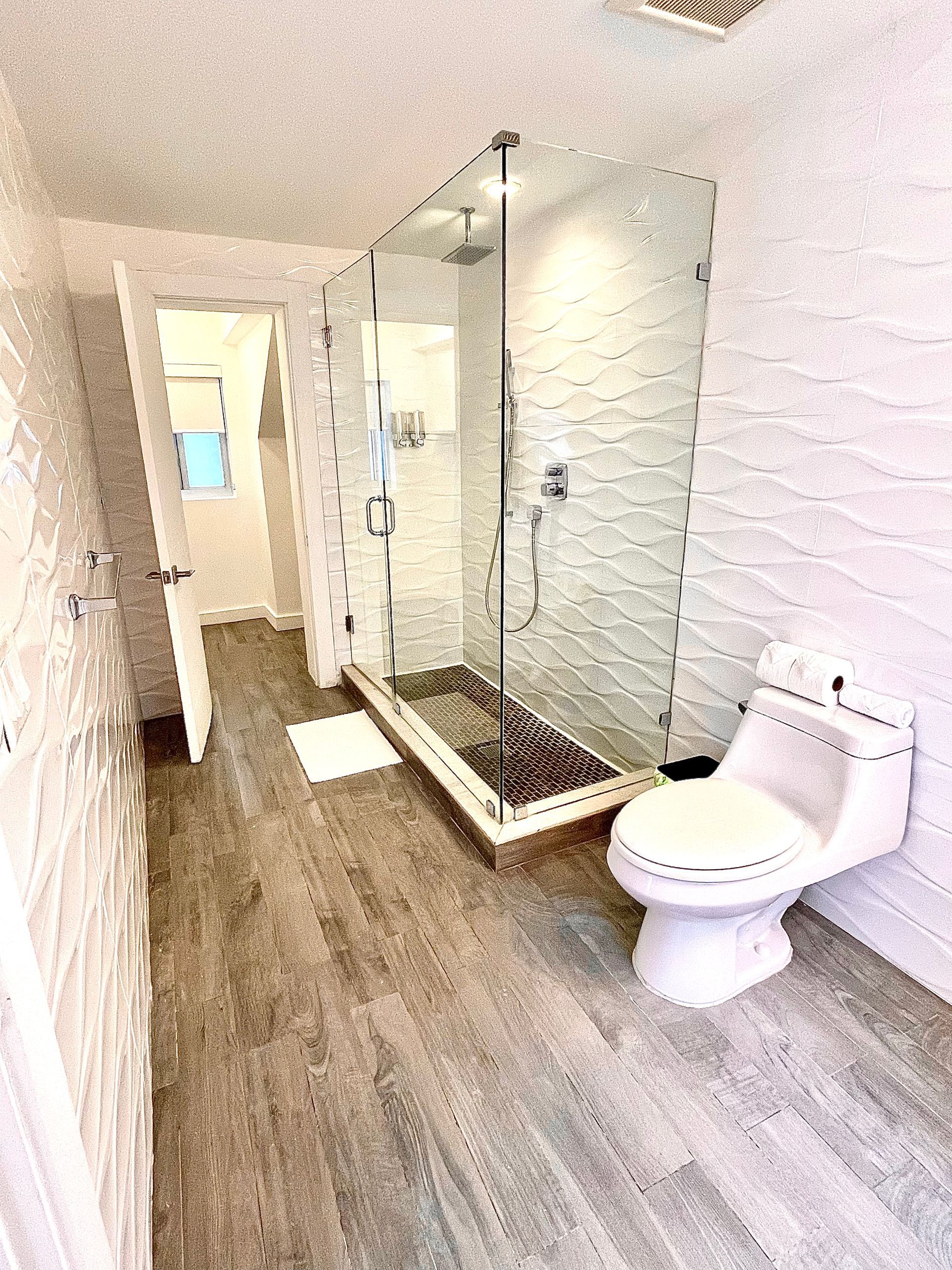 Bathroom with glass shower, toilet, and textured white and gray walls.