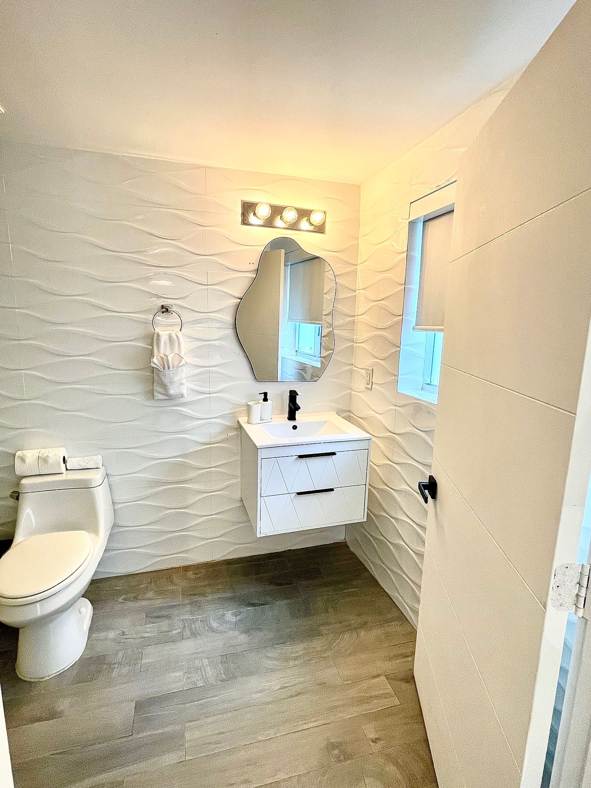 White bathroom with floating vanity, wavy wall tile, and toilet.