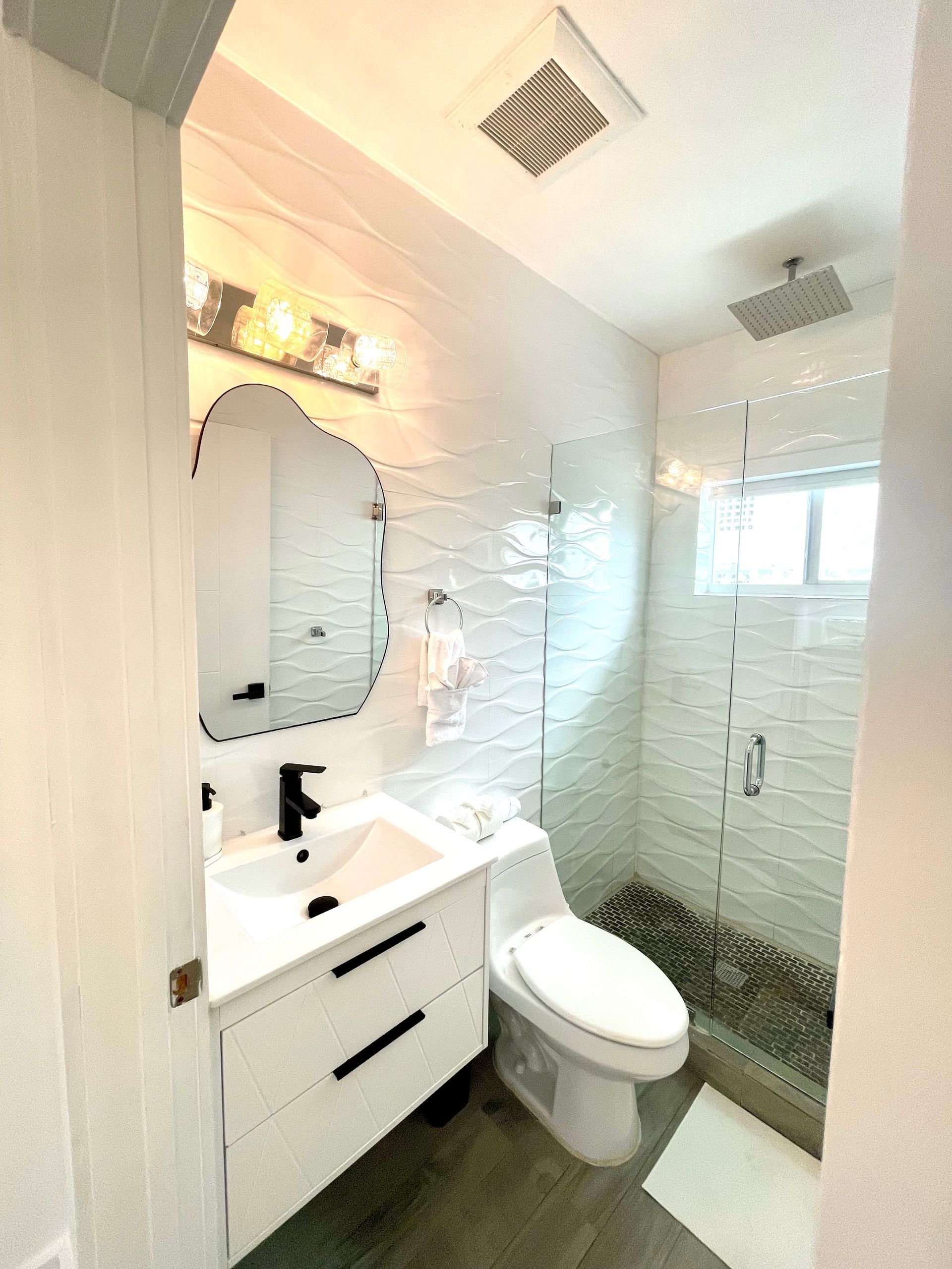 White bathroom with a modern vanity, shower, and toilet.