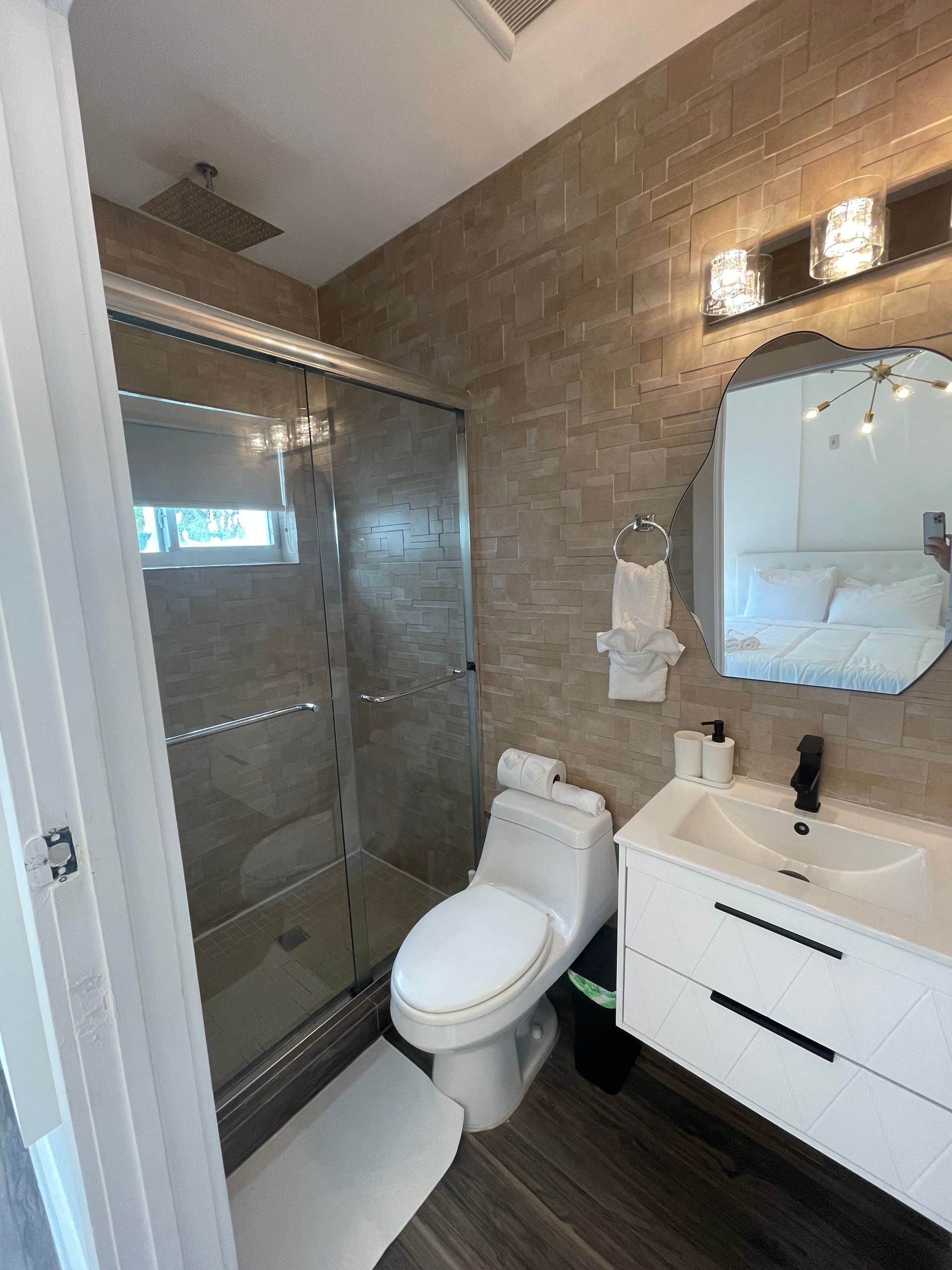 Modern bathroom with a glass shower, toilet, white sink, and textured beige wall.
