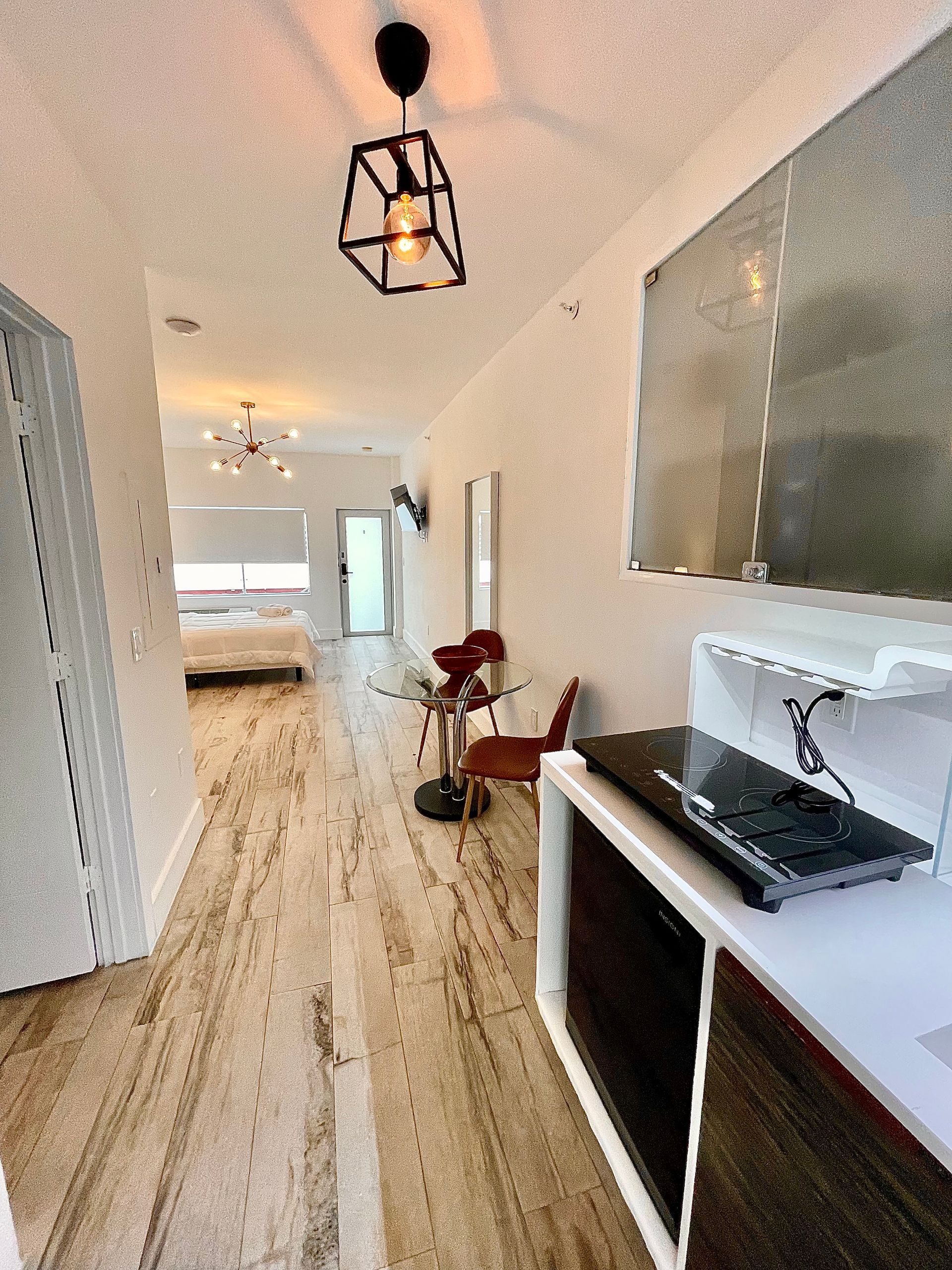 Hallway with light wooden floor, white walls, a table, and a bed in the background.