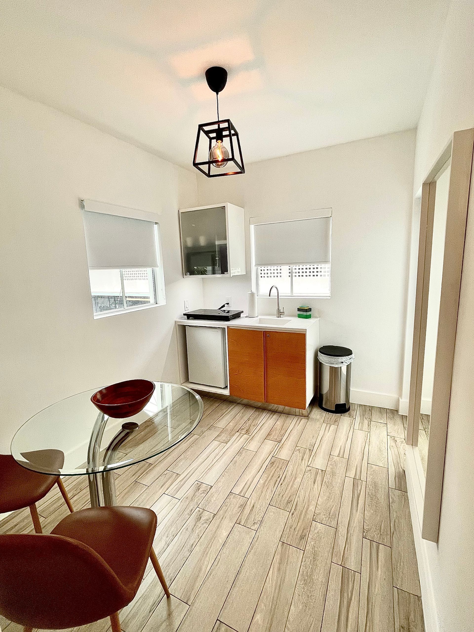 Small kitchen with dining area: white walls, wooden cabinets, glass table, pendant light.