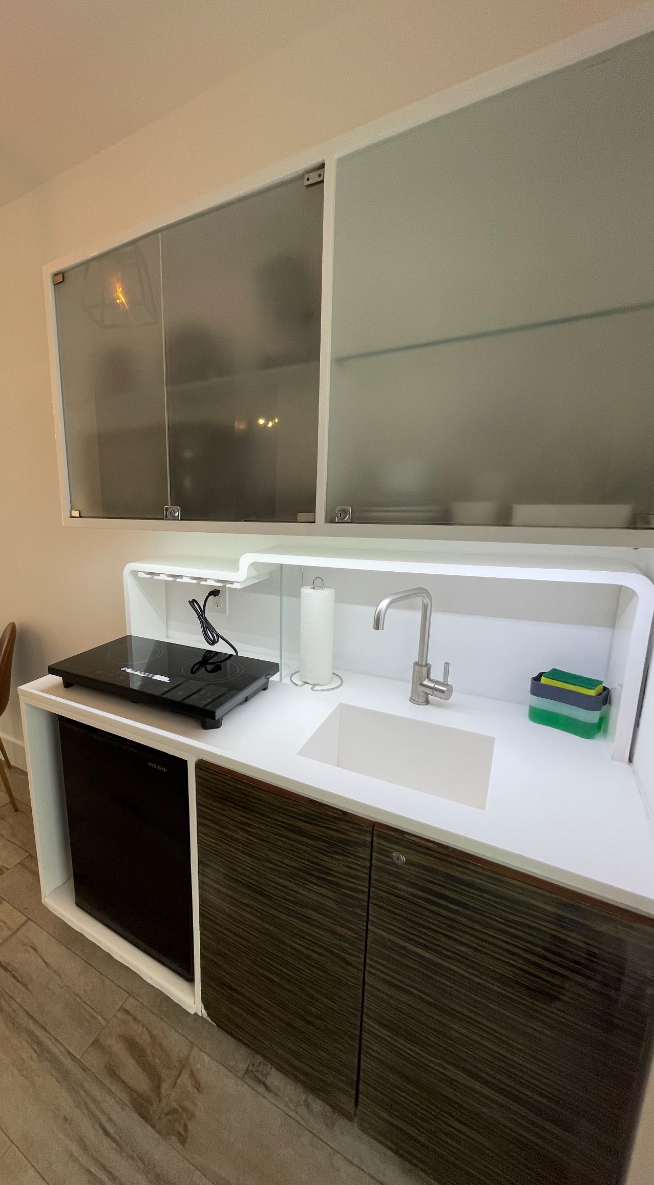 Small kitchen with a sink, stovetop, and cabinets; white countertop and upper cabinets; brown cabinet doors.