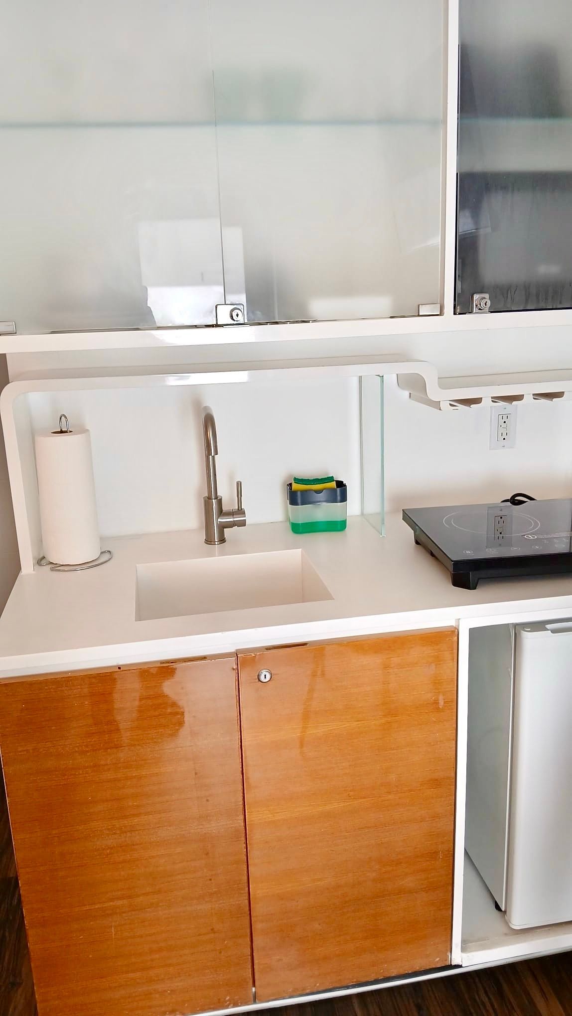 Small kitchenette with a sink, countertop burner, and mini-fridge, with white and wood cabinetry.