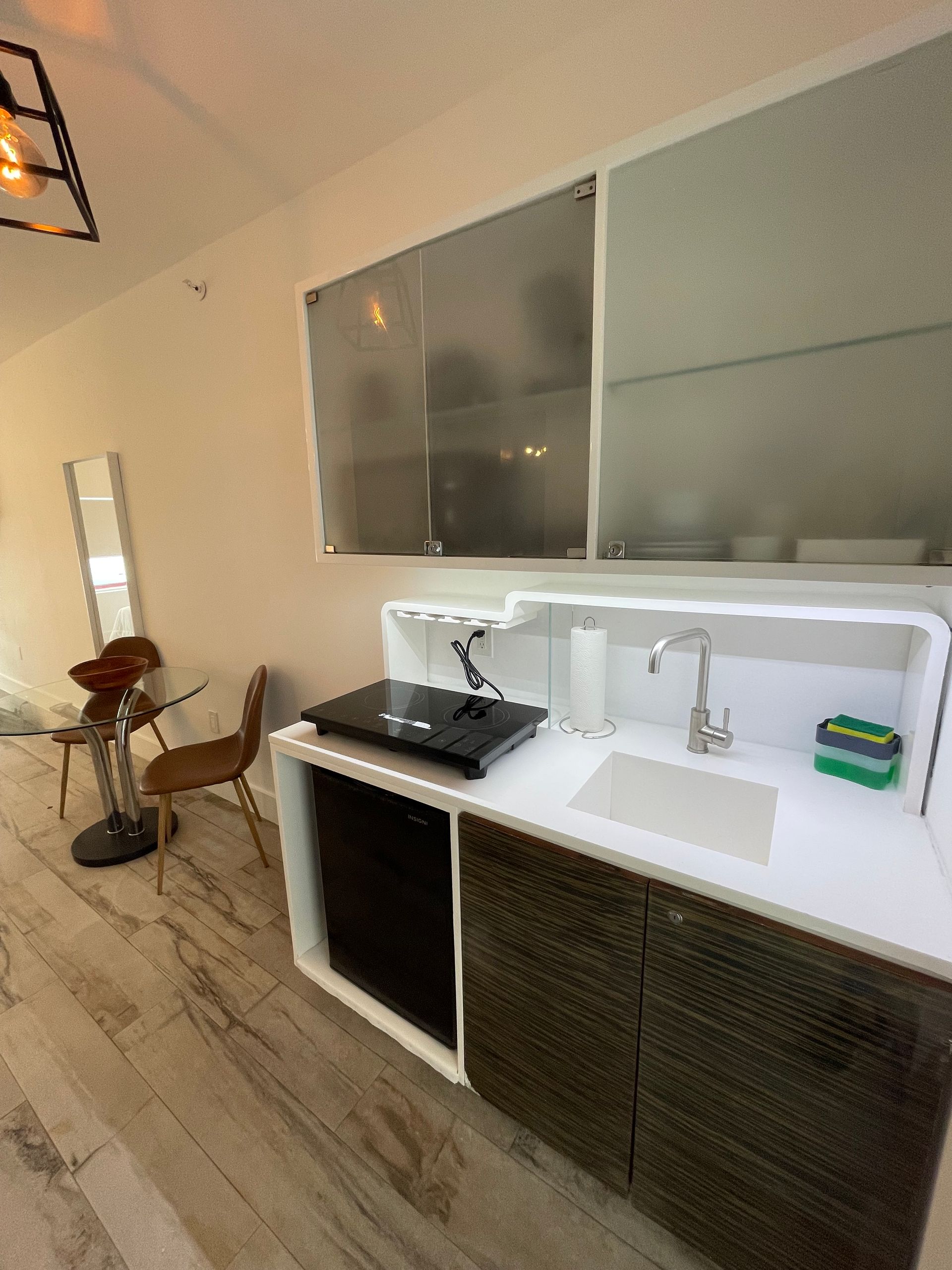 Kitchenette with countertop, sink, and cabinet with a small table and chair in the corner.